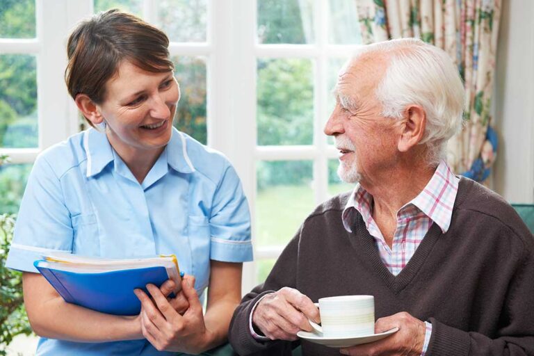 An older adult smiling while chatting with friends during an activity in a spacious common room.